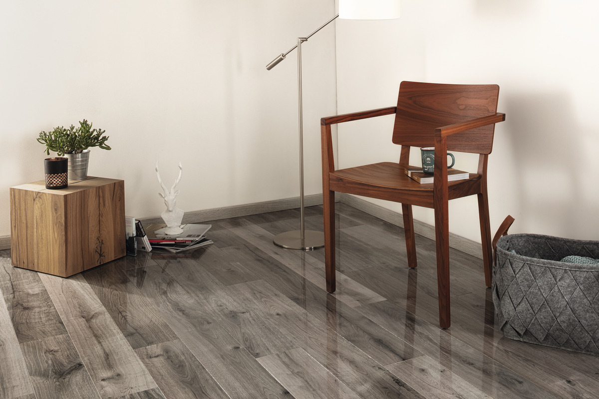 Ein Raum mit hellem Boden in Holzoptik, holzfarbenem Beistelltisch, Sessel und Wandgestaltung.