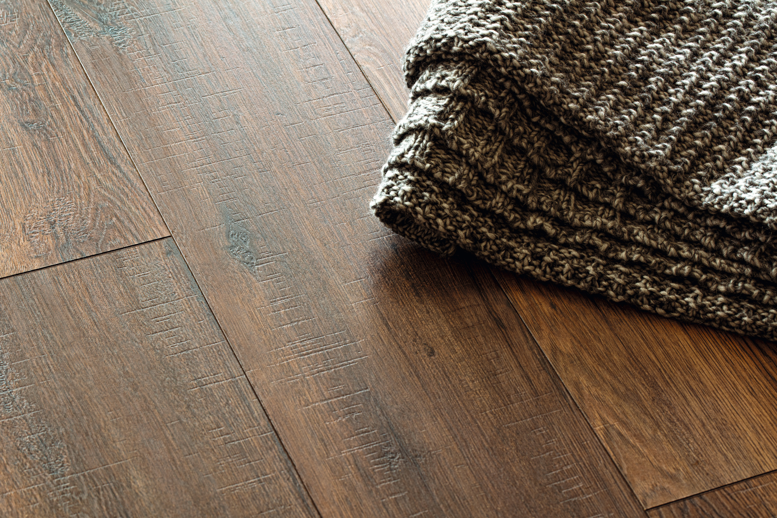 Dunkler Holzoptik Bodenbelag mit strukturierter Oberfläche, kombiniert mit einem Stricktextil für Wandgestaltung und Bodenabschluss.