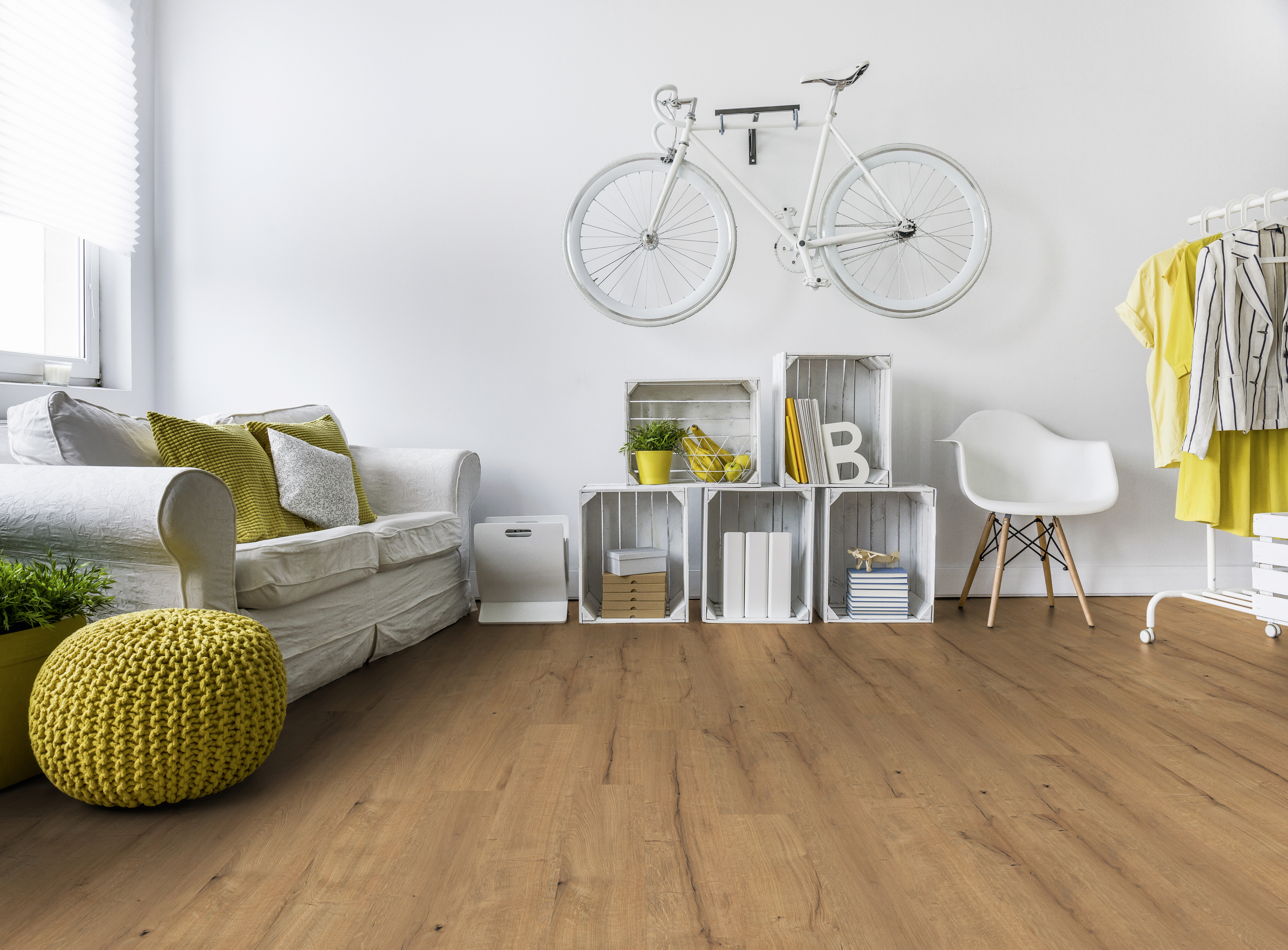 Die stilvolle Raumgestaltung zeigt einen Bodenbelag in Holzoptik, eine weiße Couch und dekorative Wandgestaltung mit weißem Fahrrad.