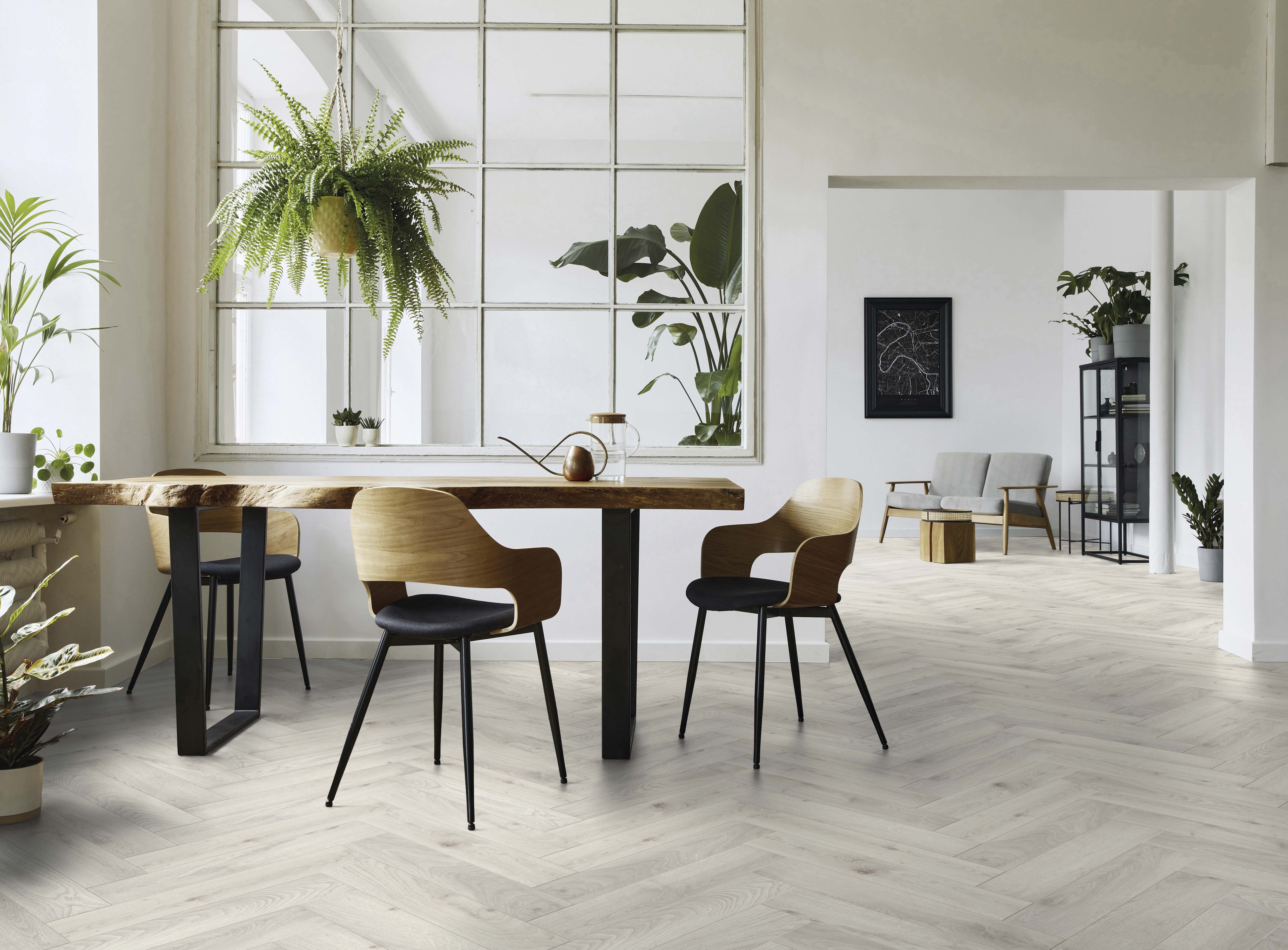 Heller Laminatboden in Fischgrätmuster verlegt, in einem Essbereich mit Holztisch und Stühlen sowie Pflanzen und Fenstergestaltung.