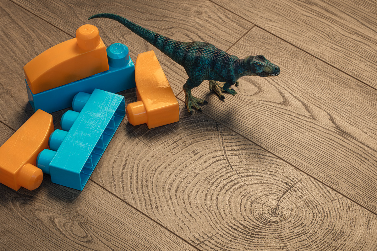 Holzboden in Eichenoptik mit deutlicher Maserung und Jahresringen, daneben Bauklötze und eine Dinosaurierfigur.