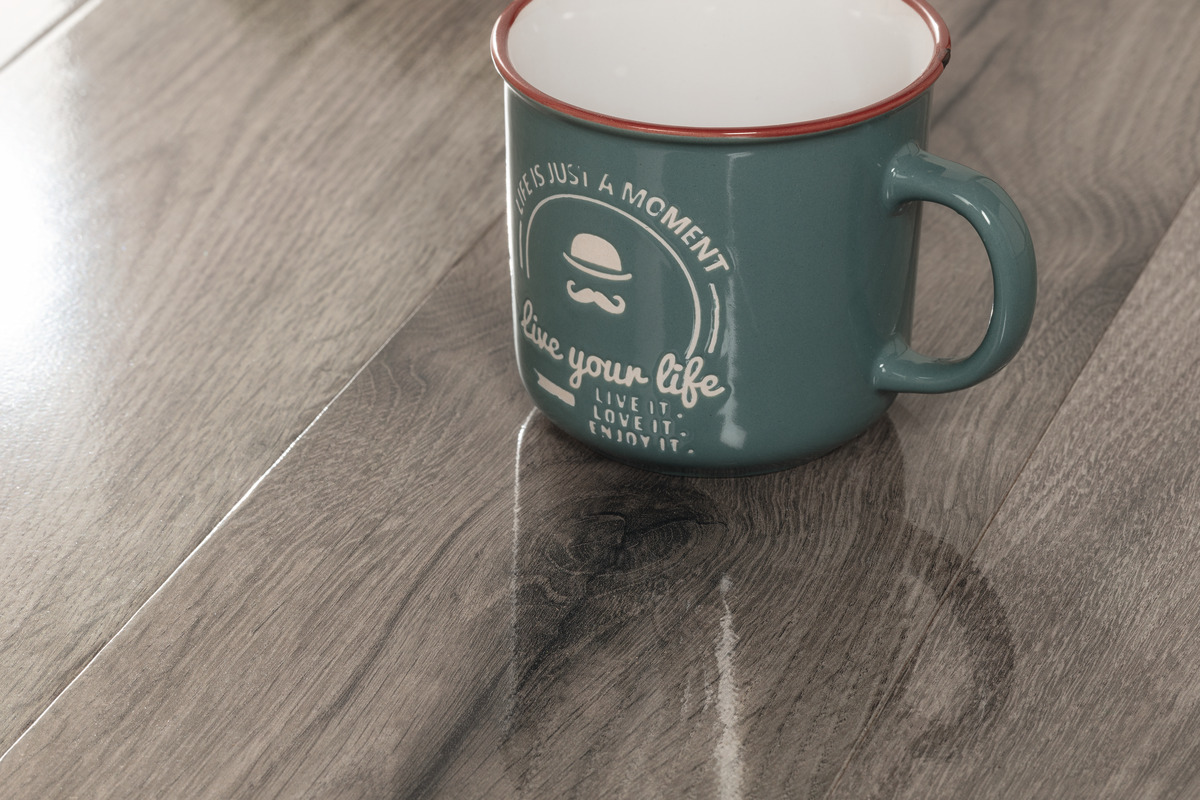 Bodenbelag in Holzoptik mit detaillierter Maserung und glänzender Oberfläche, daneben eine grüne Tasse mit Aufdruck.