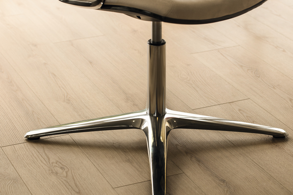 Heller Holzoptik Bodenbelag mit feiner Maserung, daneben ein chromglänzender Stuhlfuß im Detail