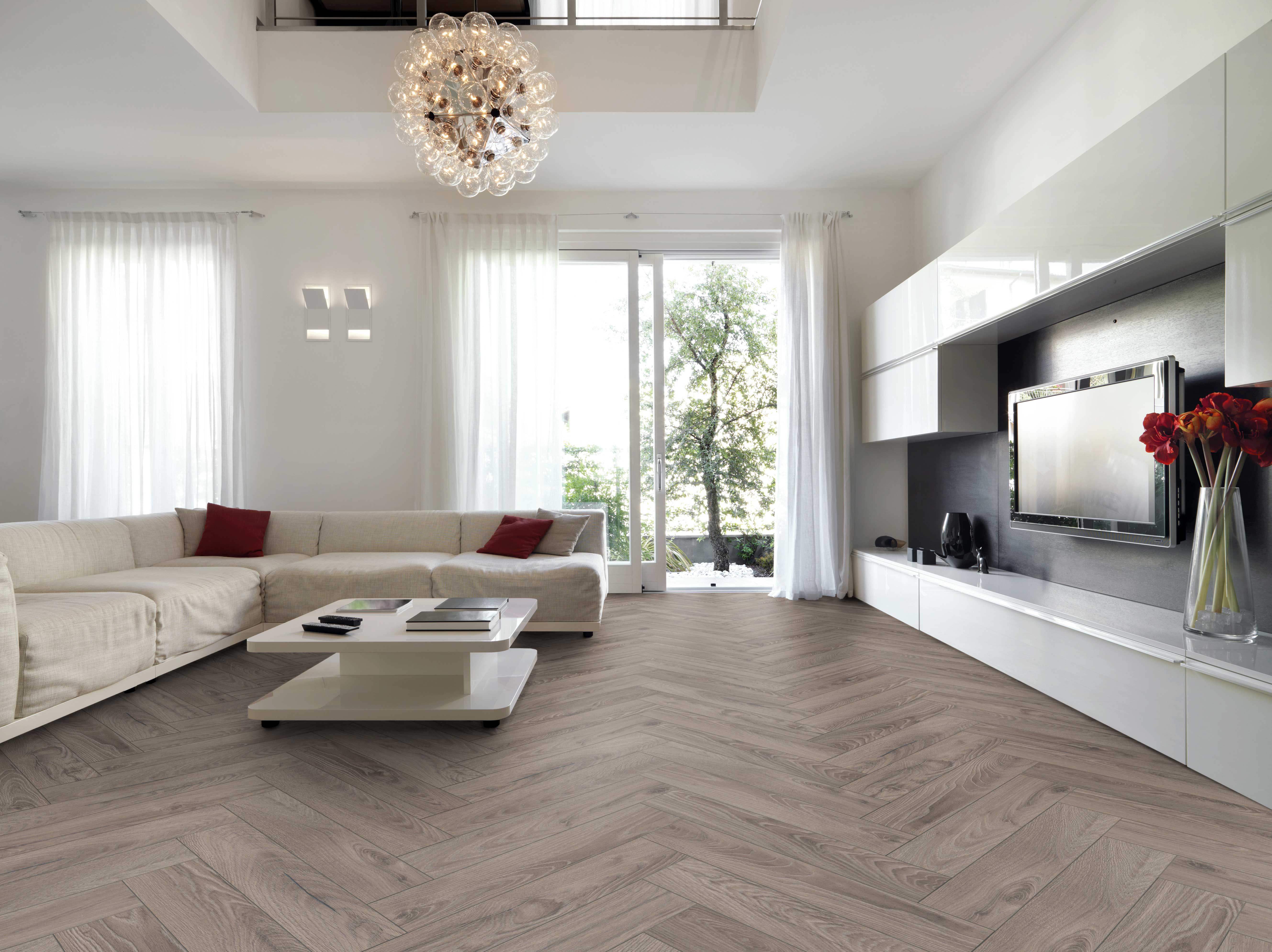 Modernes Wohnzimmer mit hellem Sofa, weißem Tisch und Bodenbelag in Holzoptik mit Fischgrätmuster.
